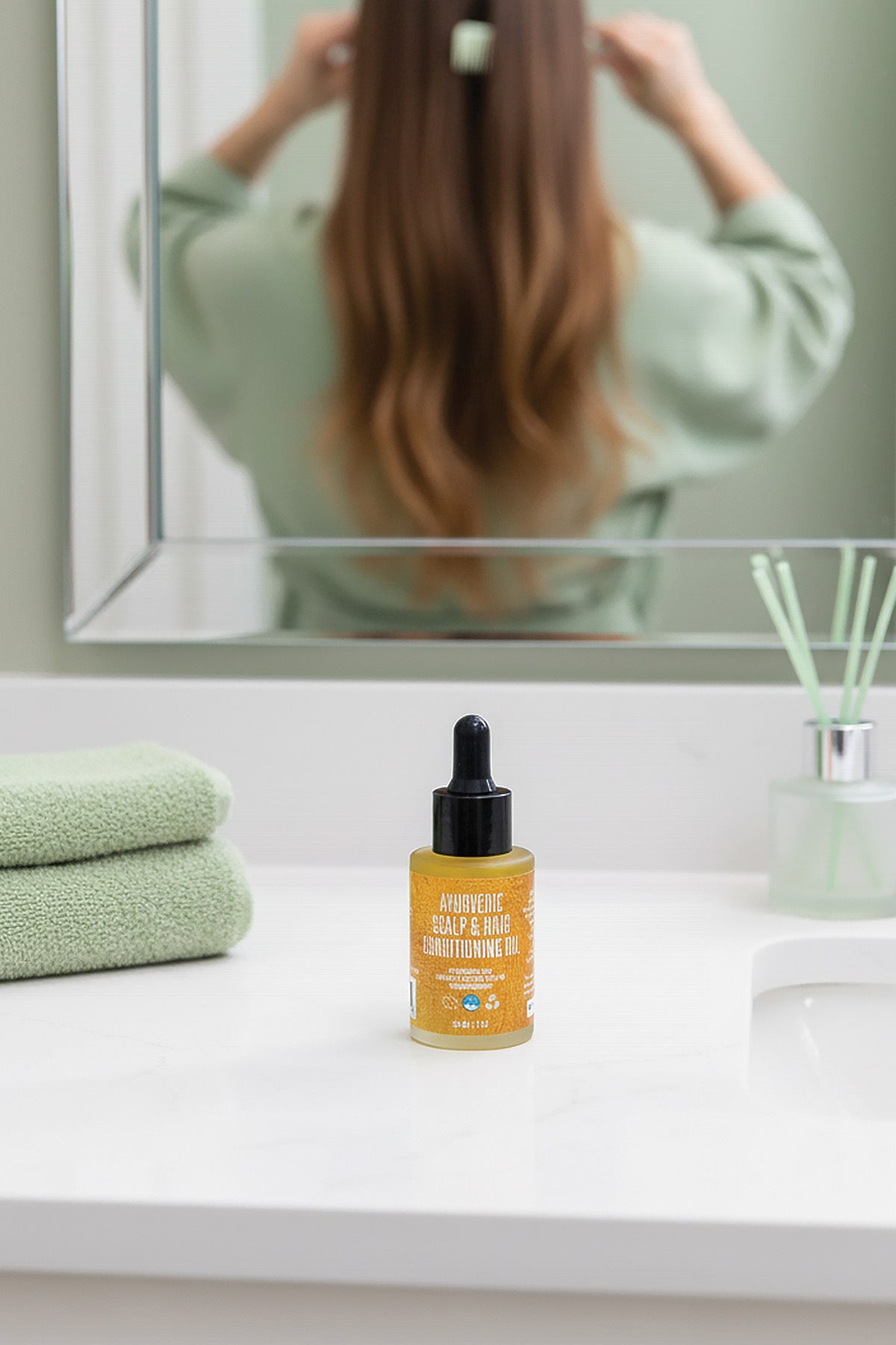Bottle of hair care product on a bathroom counter with a person styling hair in the background