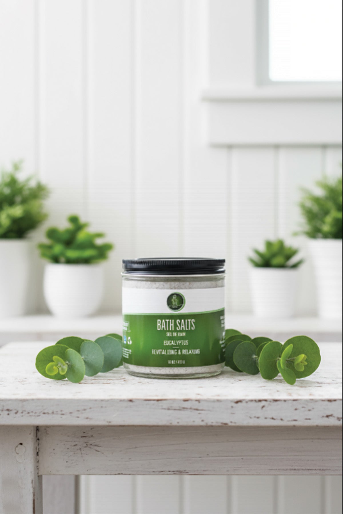 Bath salts container with green label on a white surface with plants in the background