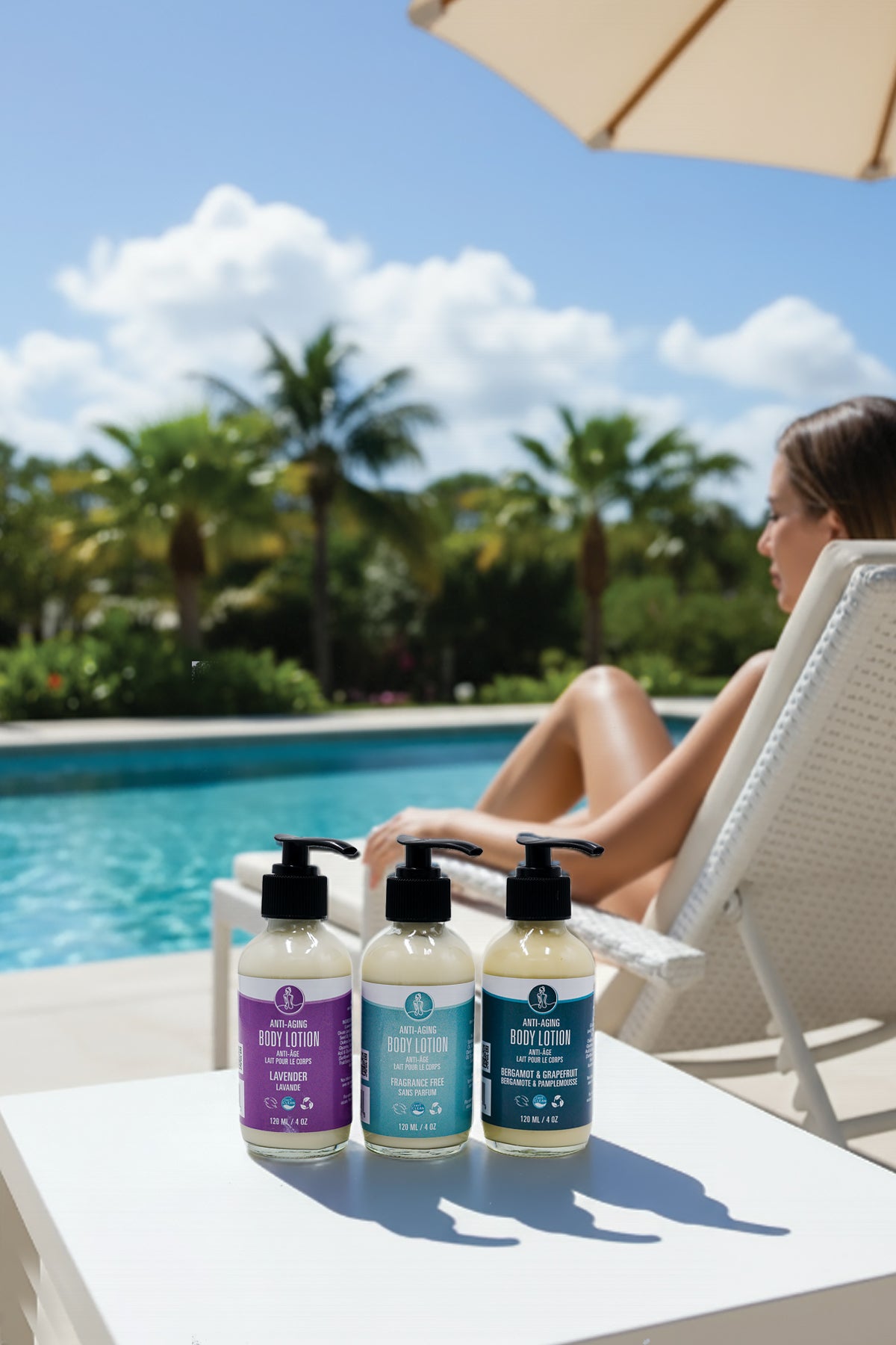 Three bottles of body lotion on a table by a pool with a person sitting in the background.