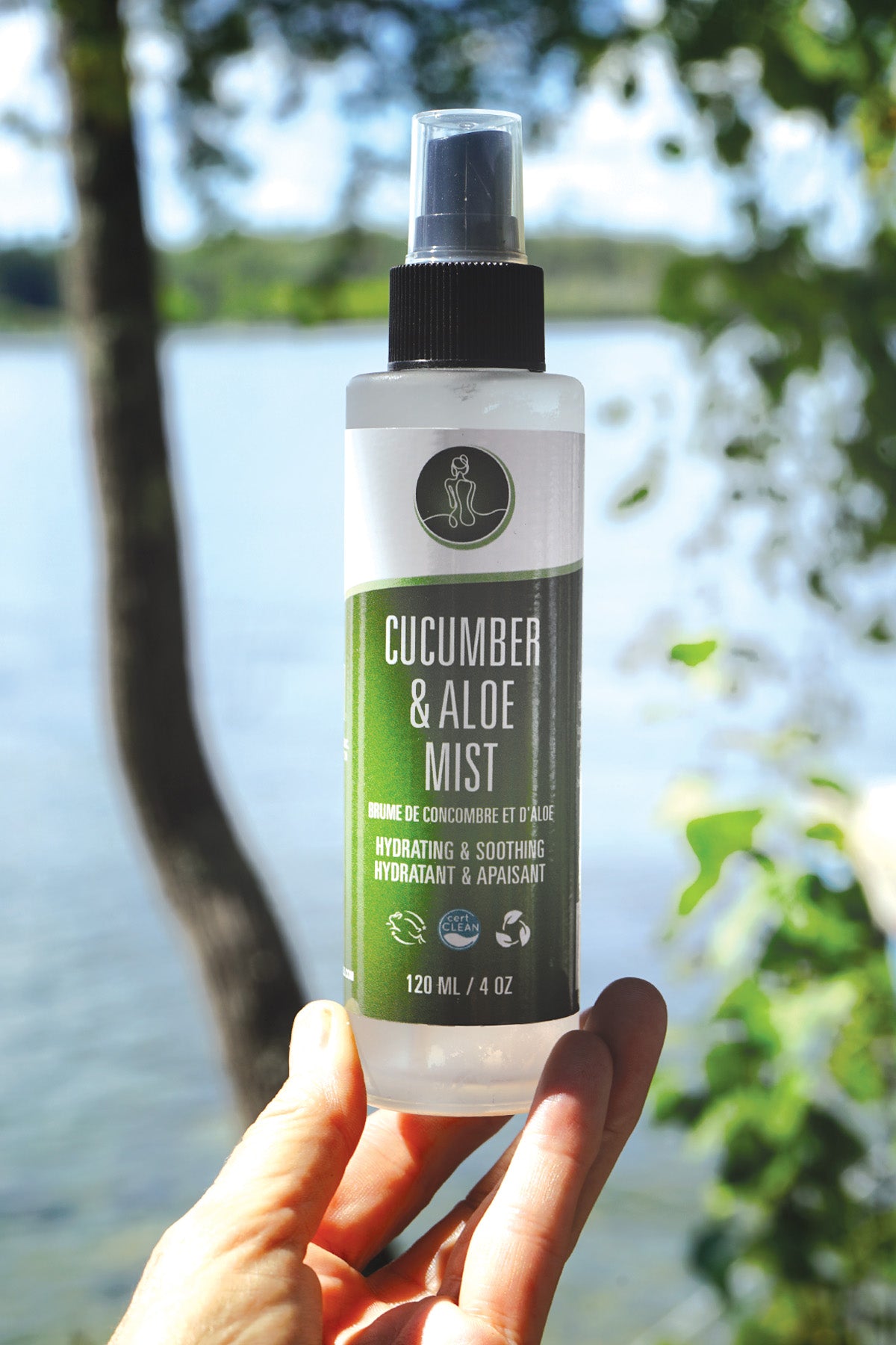 Cucumber & Aloe Mist bottle held in front of a natural background with water and trees.