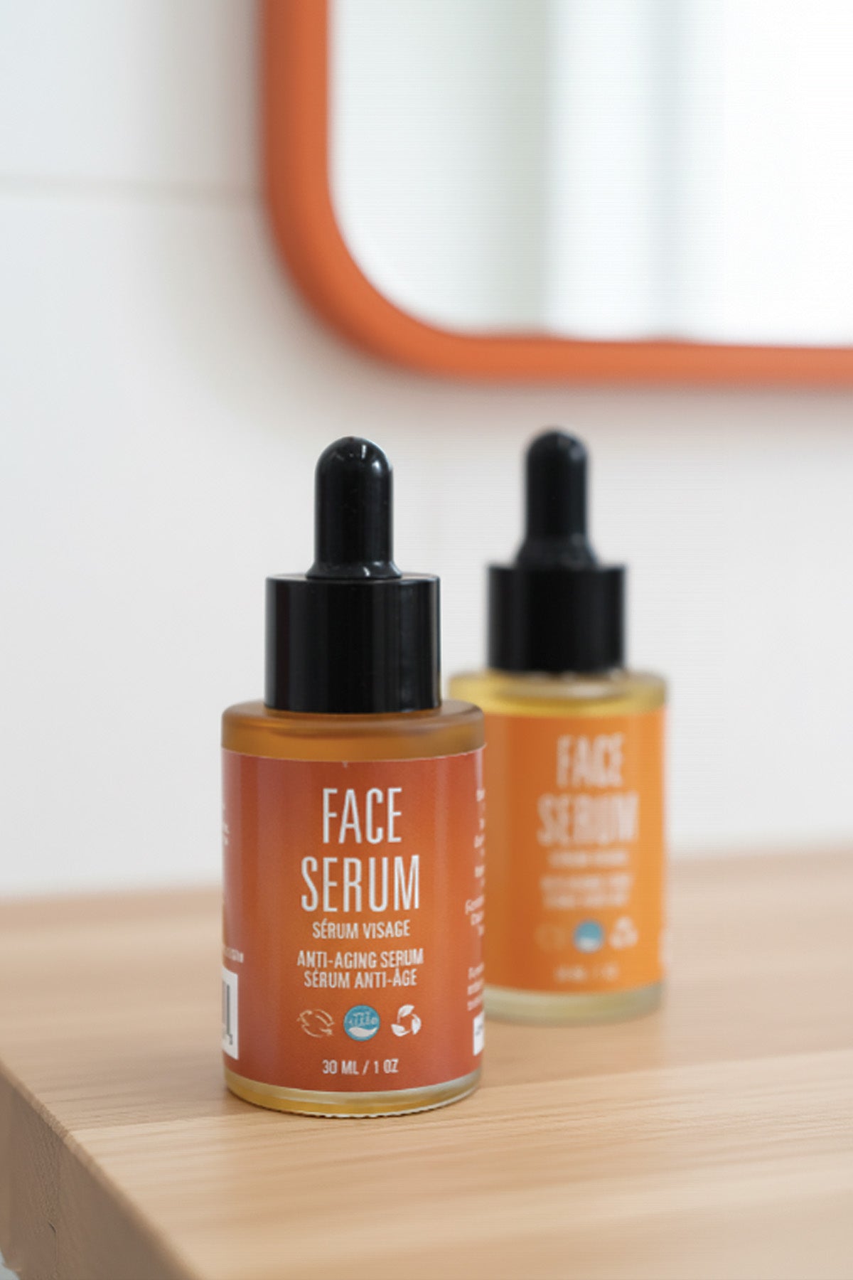 Two bottles of face serum on a wooden surface with a mirror in the background.
