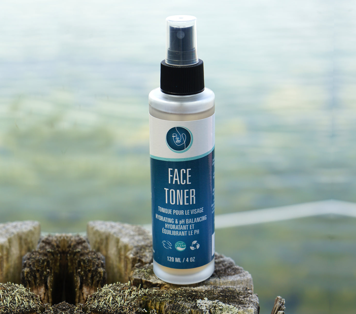 Face toner spray bottle on a wooden log with a blurred natural background Pure Heart Essentials