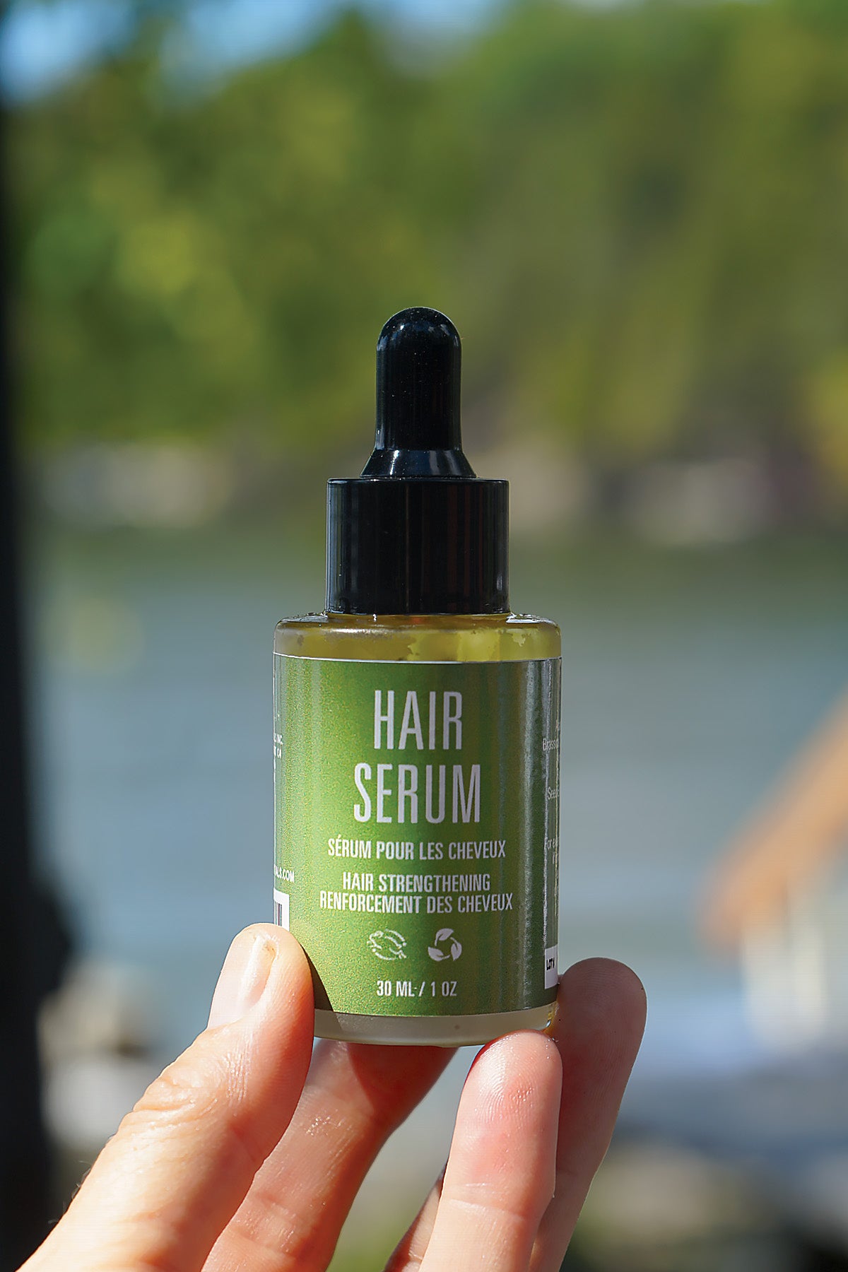 Hand holding a bottle of hair serum with a blurred natural background