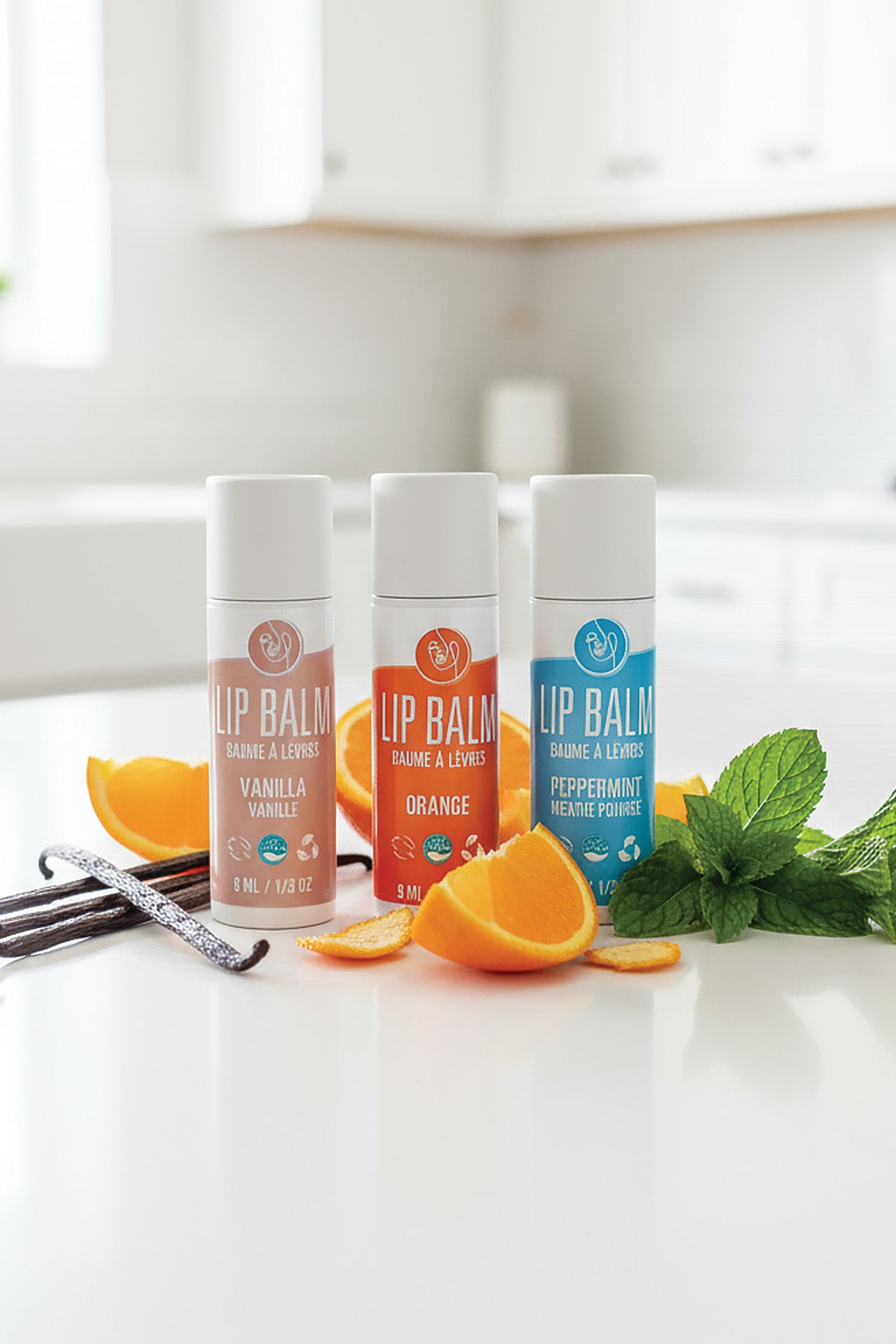 Three lip balm tubes with orange slices and mint leaves on a white surface.