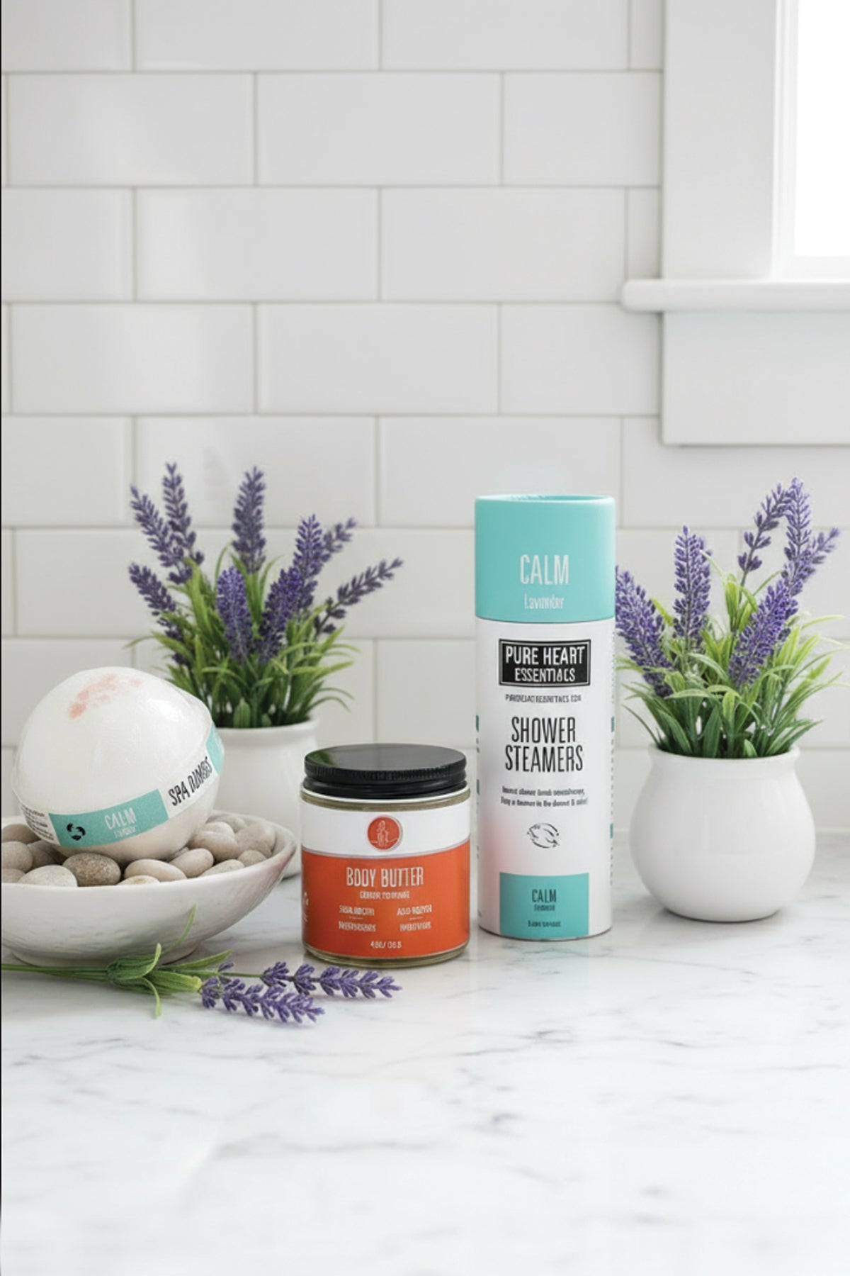 Bathroom setting with bath bombs, candles, and lavender plants on a white countertop.