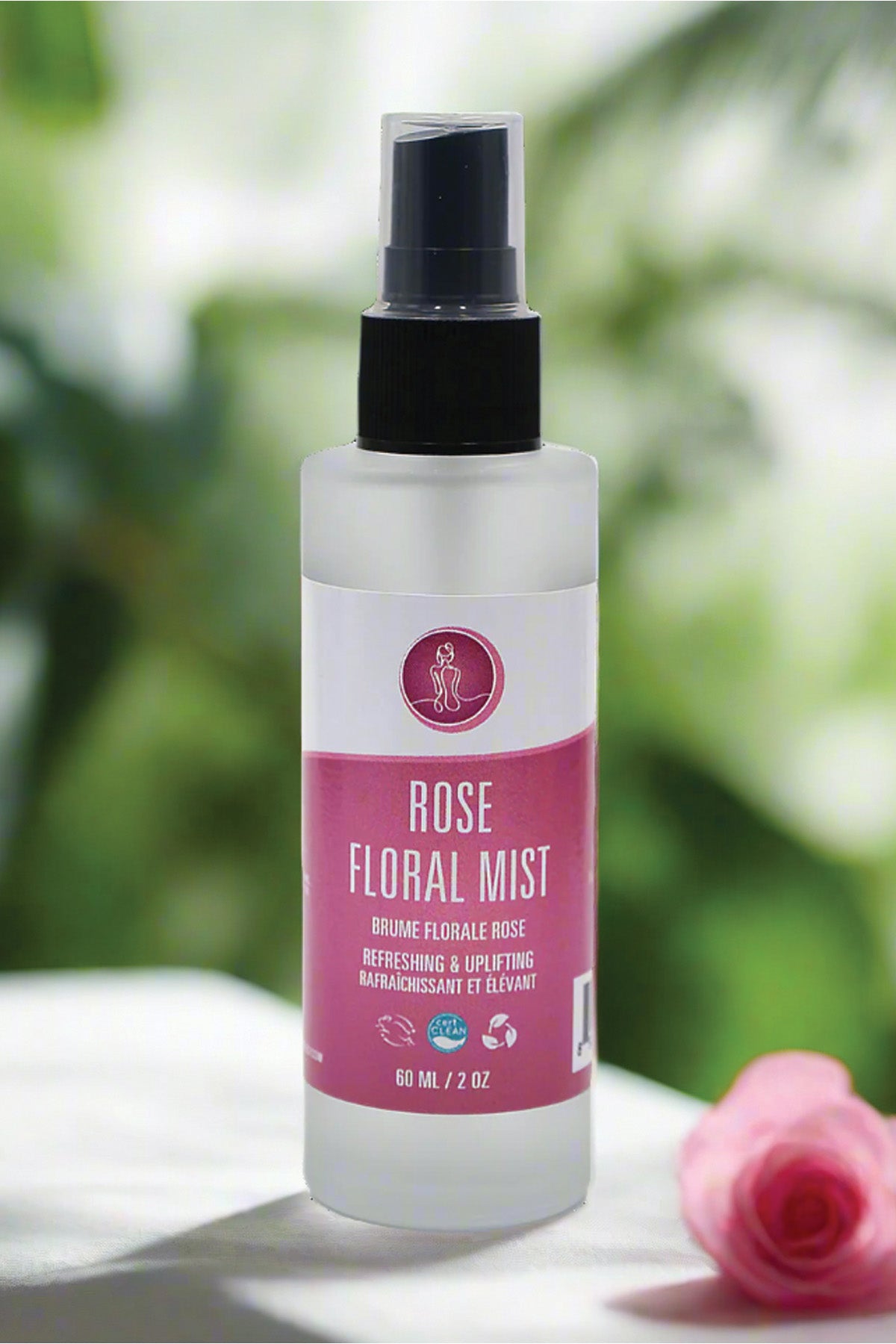 Rose floral mist spray bottle with pink label on a white surface with blurred green background