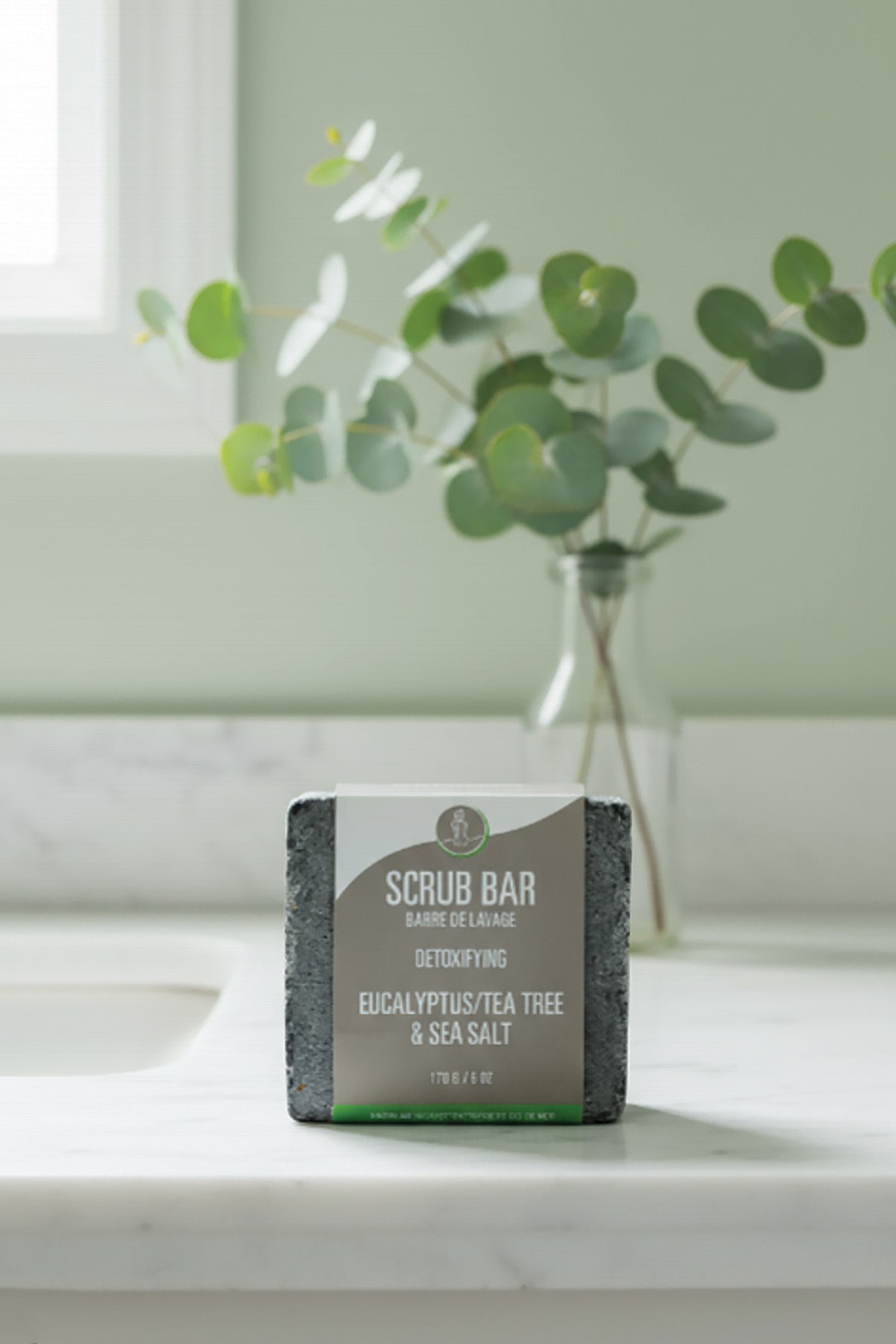 Scrub bar on a bathroom counter with a vase of eucalyptus in the background