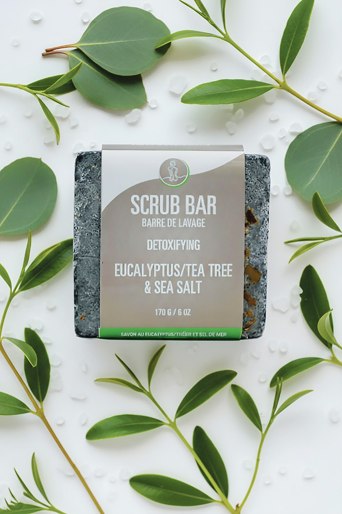 Scrub bar with eucalyptus, tea tree, and sea salt on a white background with green leaves.