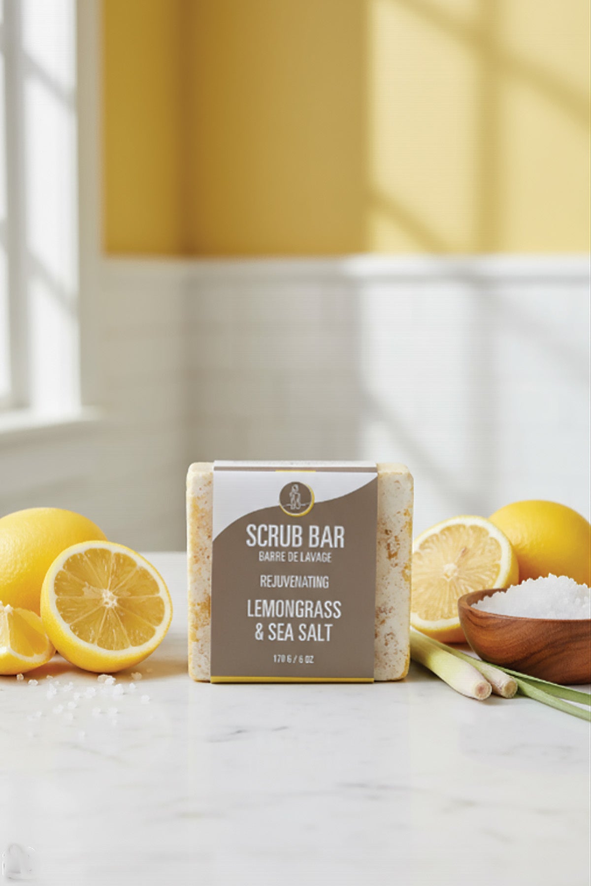 Scrub bar with lemongrass and sea salt on a white surface with lemons and a bowl of salt.