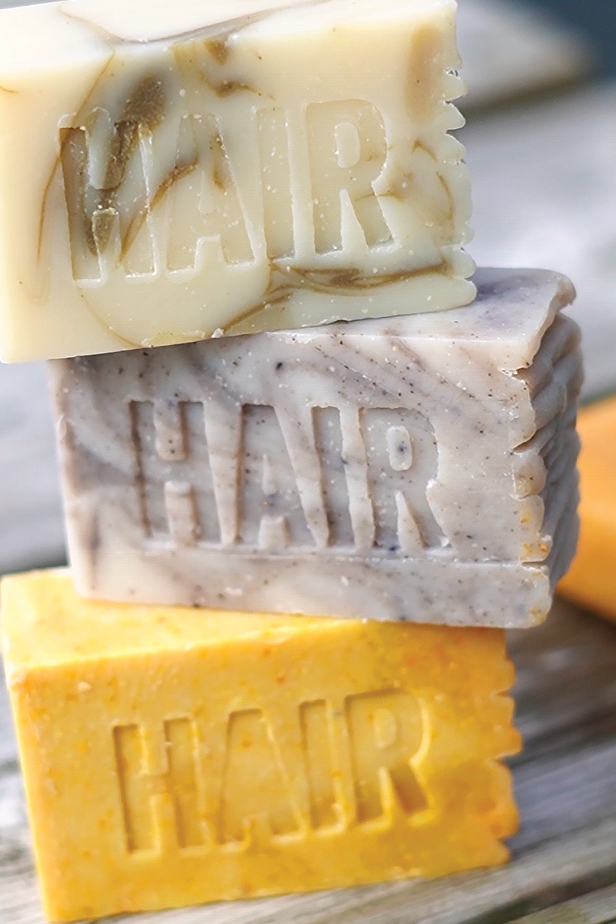 Three shampoo bars with 'HAIR' branding stacked on a wooden surface.
