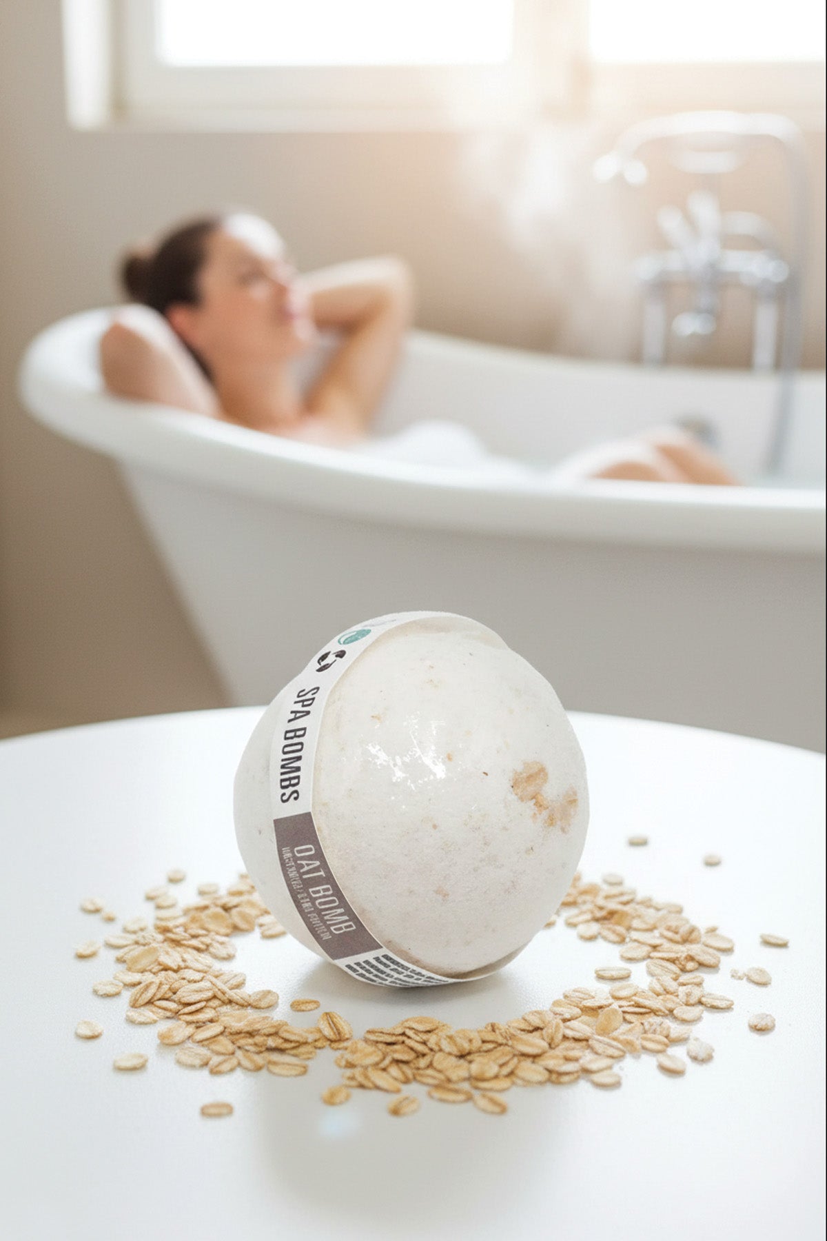 Bath bomb with oats on a table in front of a bathtub with a person relaxing inside.