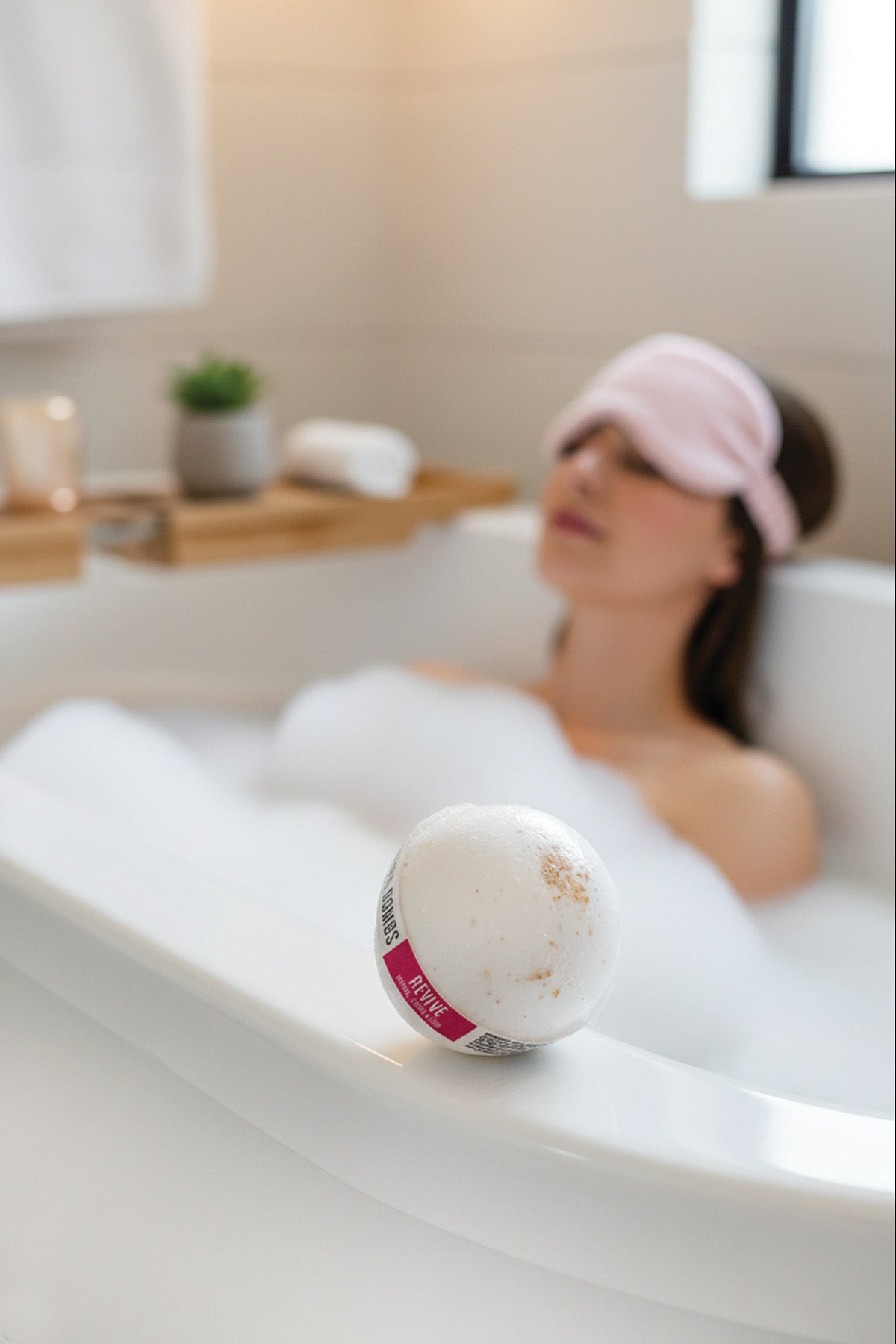 Woman relaxing in a bubble bath with a bath bomb in the foreground.