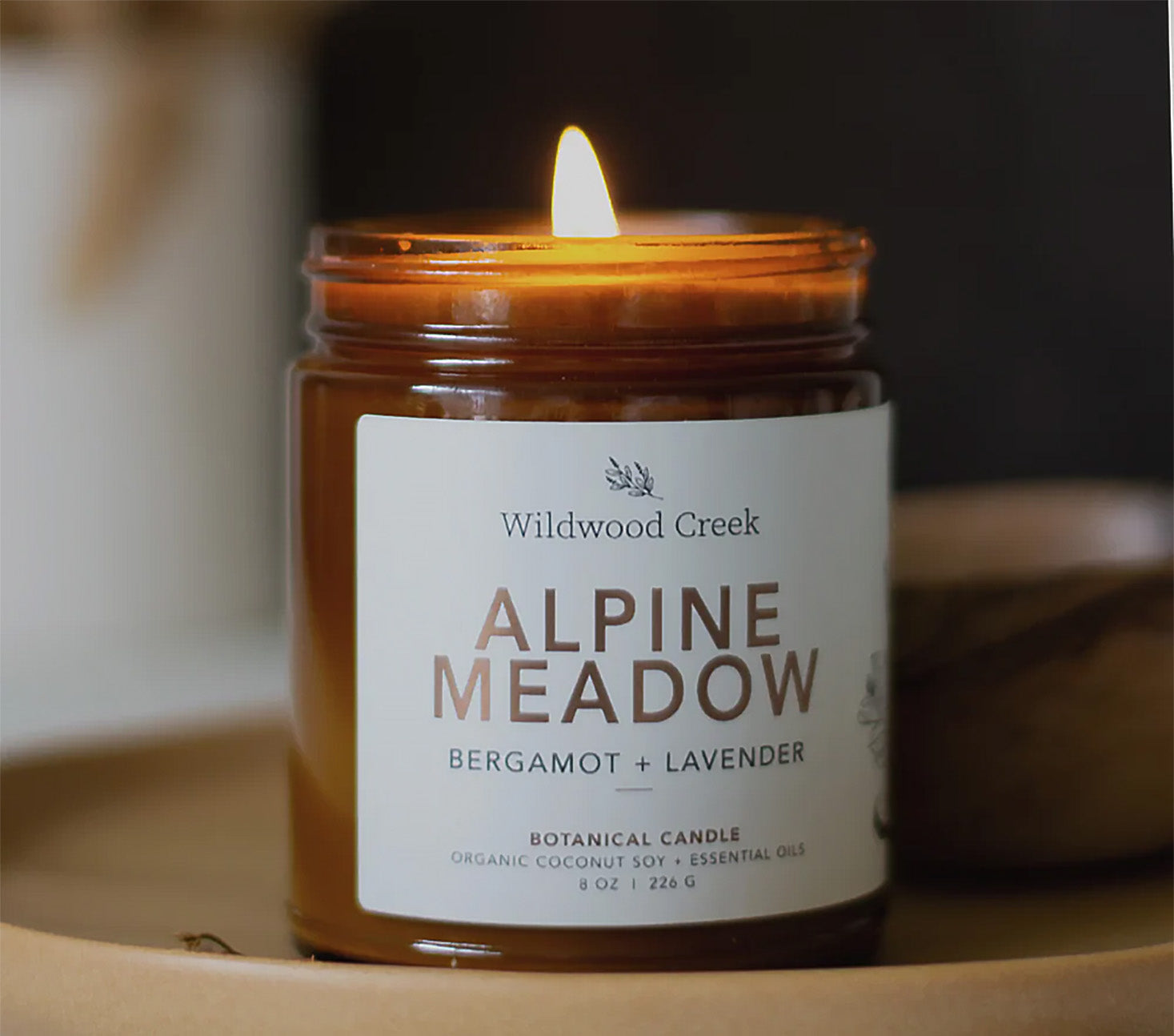 Candle labeled 'Alpine Meadow' by Wildwood Creek with a flame on a dark background